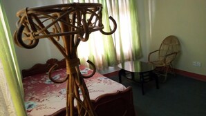 A room with a bed, a round table, a wicker chair, and a curtain. - Shree yoga retreat (Kathmandu)