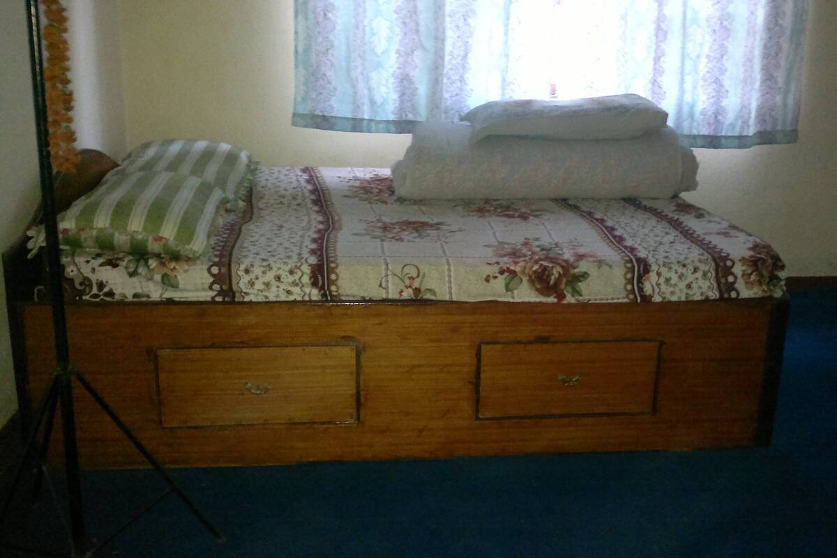 A wooden bed with floral bedding, a window with lace curtains, and a blue carpet.