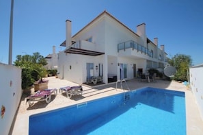 A two-story house with a swimming pool, a covered patio, and a satellite dish.