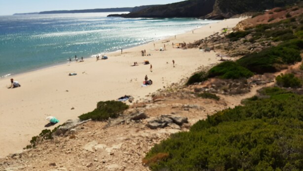 A beach with people, a clear sky, and a rocky hillside.