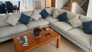 A living room with a grey sectional sofa, a wooden coffee table, and a staircase in the background.