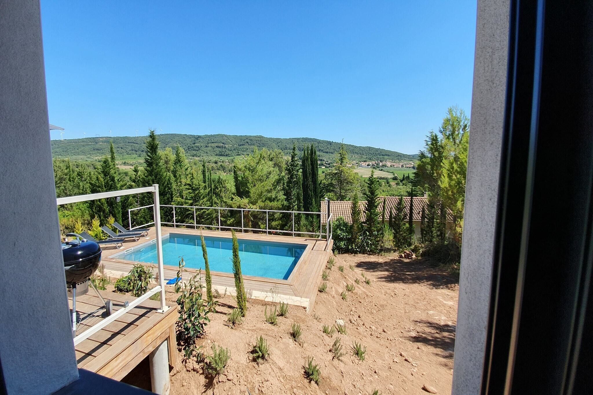 A swimming pool with a wooden deck, surrounded by greenery and hills in the background.