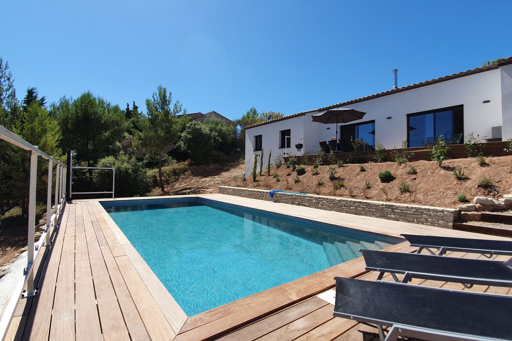 A modern house with a wooden deck, a swimming pool, and a patio area with outdoor furniture.