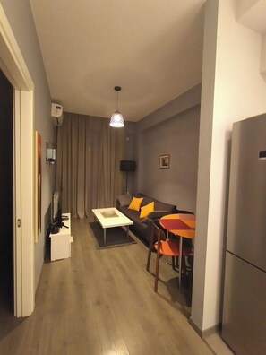 A compact living space with a sofa, a coffee table, a dining table with chairs, a ceiling light, and a refrigerator. - cozy new stylish Tbilisi view apartment -self check in free Wi-fi (Vake-Saburtalo)
