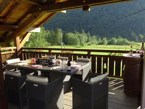 A wooden deck with a table set for dining, overlooking a forested valley.