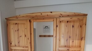 Un armadio in legno con anta a specchio, dotato di diversi cassetti e un'asta appendiabiti.