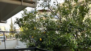 A balcony with a table and chairs, surrounded by greenery and a building in the background. - Bulut Apartment (Konyaalti)
