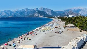 A beach with a stone wall, clear blue sea, and mountains in the background. - Bulut Apartment (Konyaalti)
