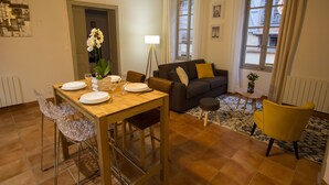 A dining area with a wooden table, chairs, and a vase of flowers. There is a sofa and a yellow armchair in the living area. - In complete privacy in the historic center (Montauban)