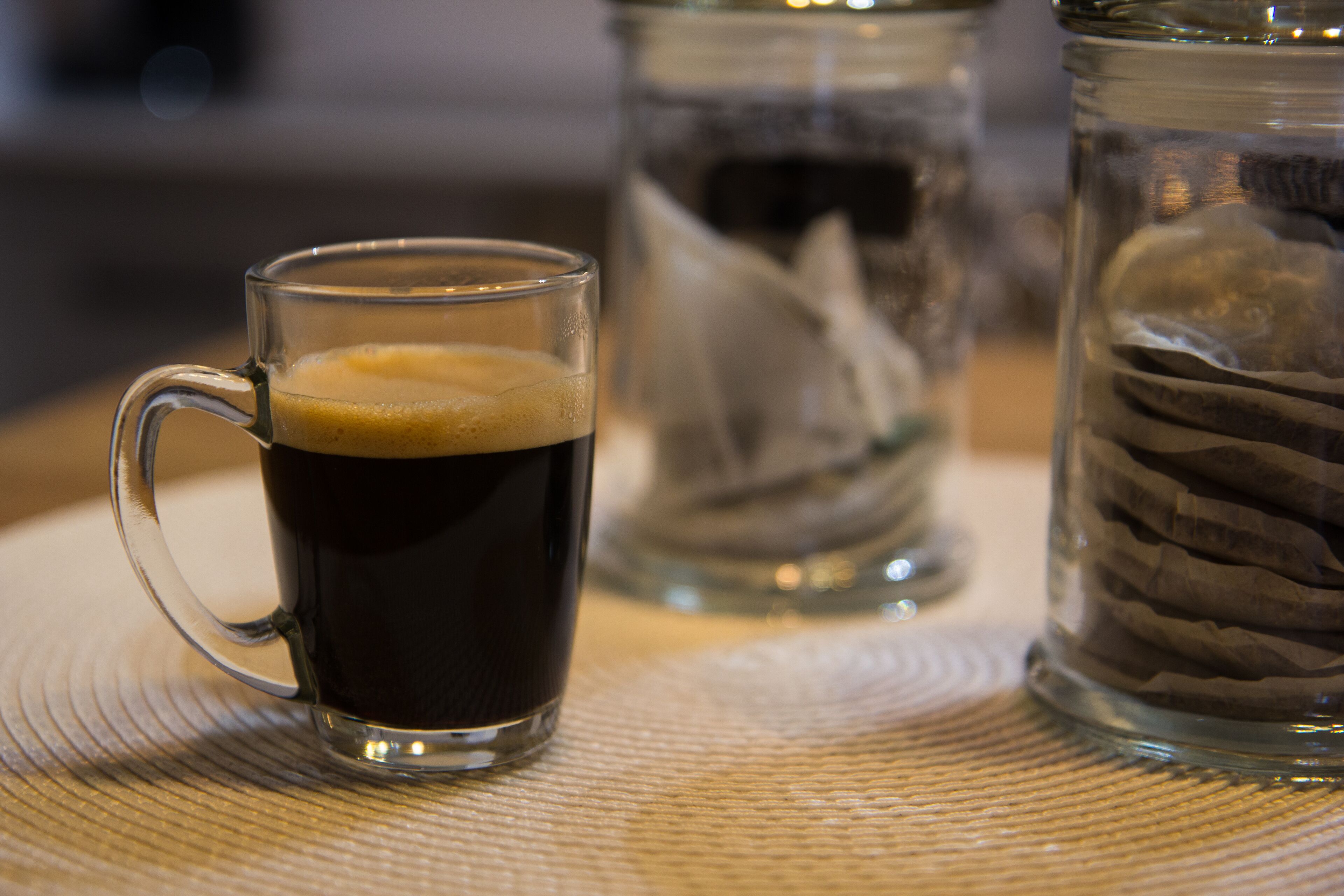Et gennemsigtigt glas krus fyldt med en mørk væske, muligvis kaffe, på en ru overflade.
