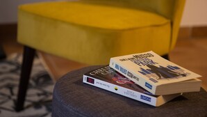 A stack of books on a grey ottoman with a yellow chair in the background. - In complete privacy in the historic center (Montauban)