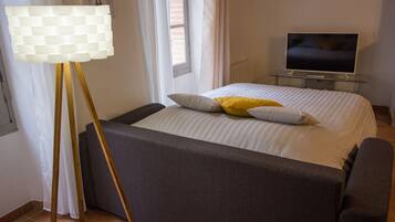 Un dormitorio con cama, televisor, lámpara y ventana.