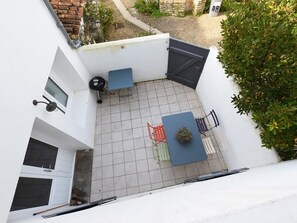 A small outdoor patio area with a tiled floor, a blue table, a red chair, and a small plant.