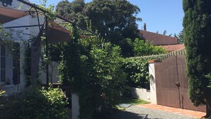 Un barrio residencial con un camino pavimentado, una casa blanca de techo rojo y un seto verde alto.