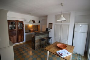Une cuisine avec un îlot central en bois, des tabourets de bar, un réfrigérateur blanc et un sol à carreaux.