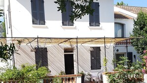 Un edificio blanco de dos pisos con techo de tejas, un patio cubierto con mobiliario exterior y un césped bien cuidado.