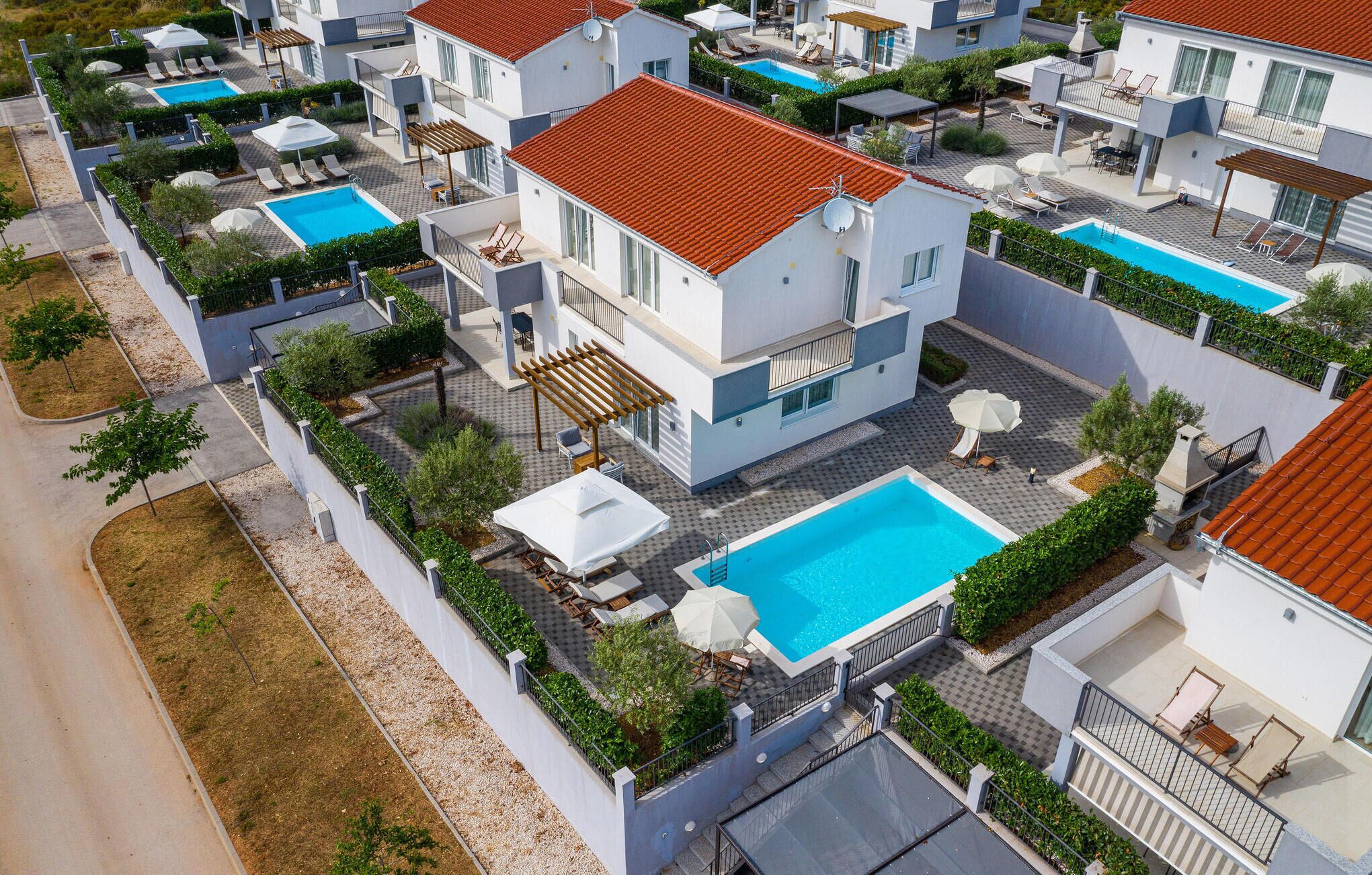 A residential complex with multiple two-story houses, each featuring a swimming pool, outdoor seating, and a garden area.