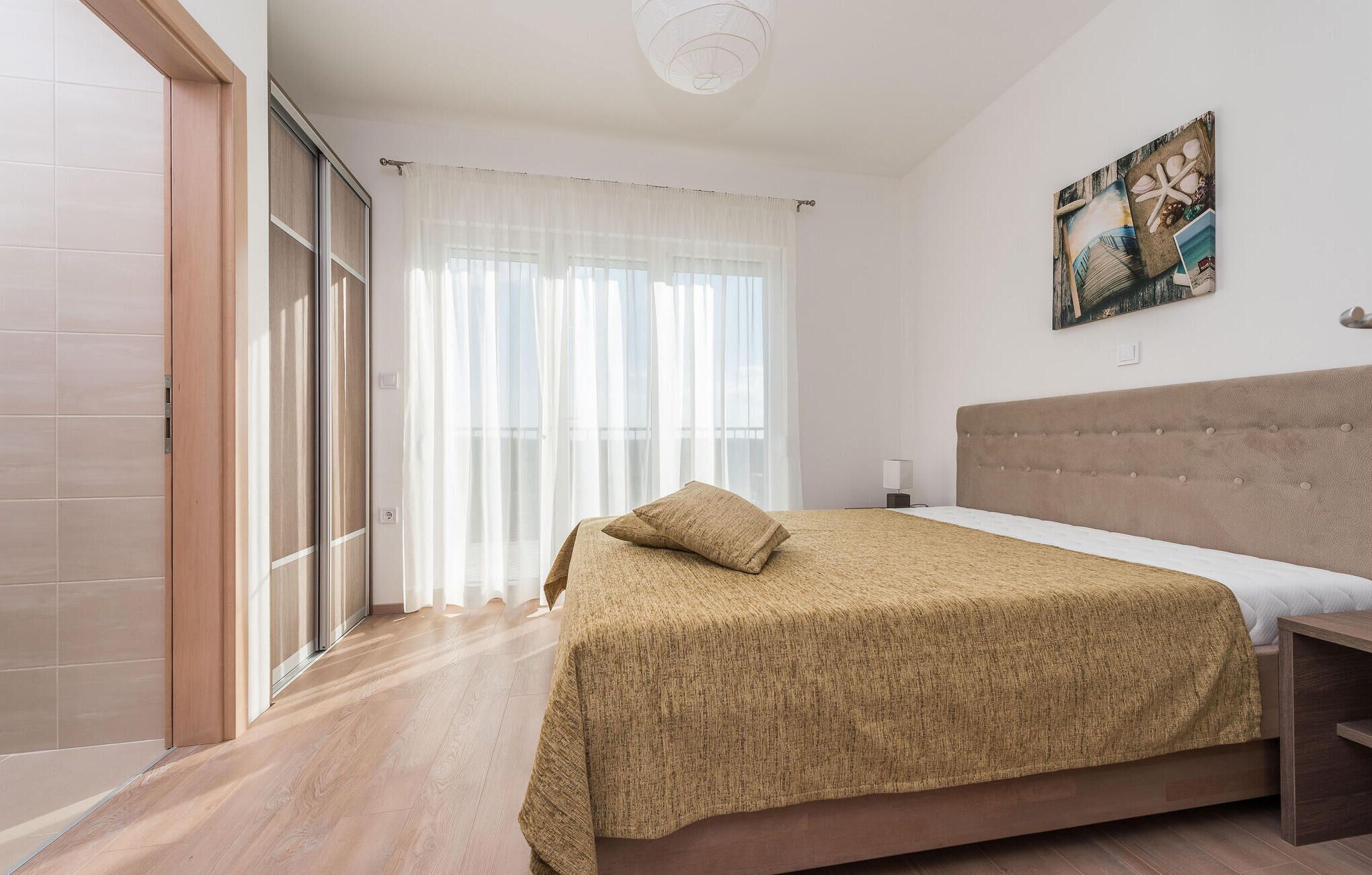 A bedroom with a bed, a headboard, a painting, and a window with curtains.