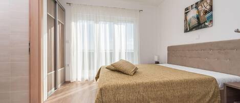 A bedroom with a bed, a headboard, a painting, and a window with curtains.