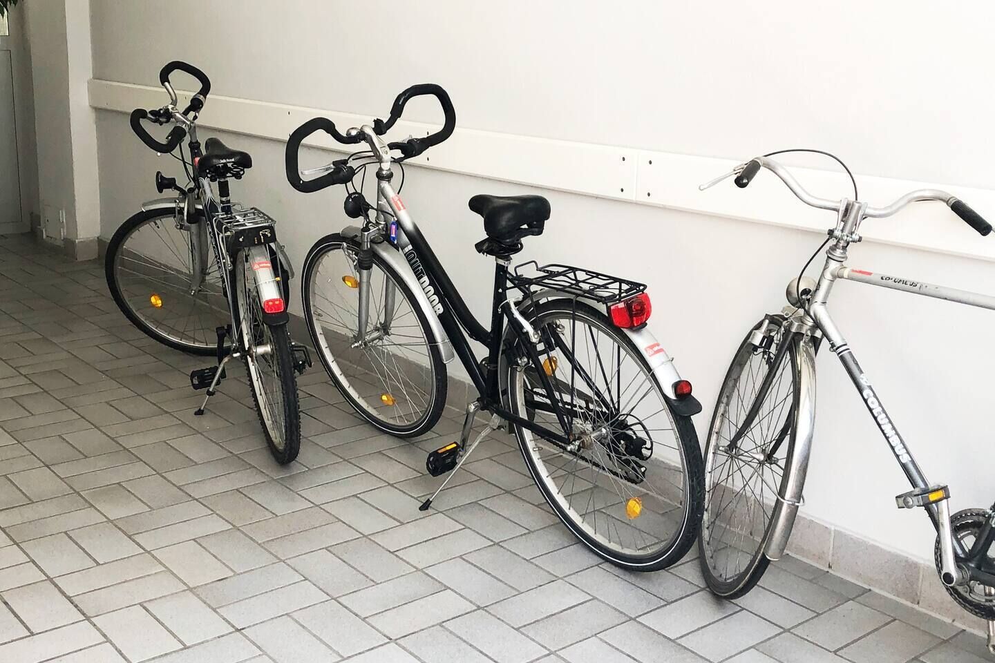 Tre biciclette appoggiate a una parete in un ambiente interno rivestito di piastrelle.