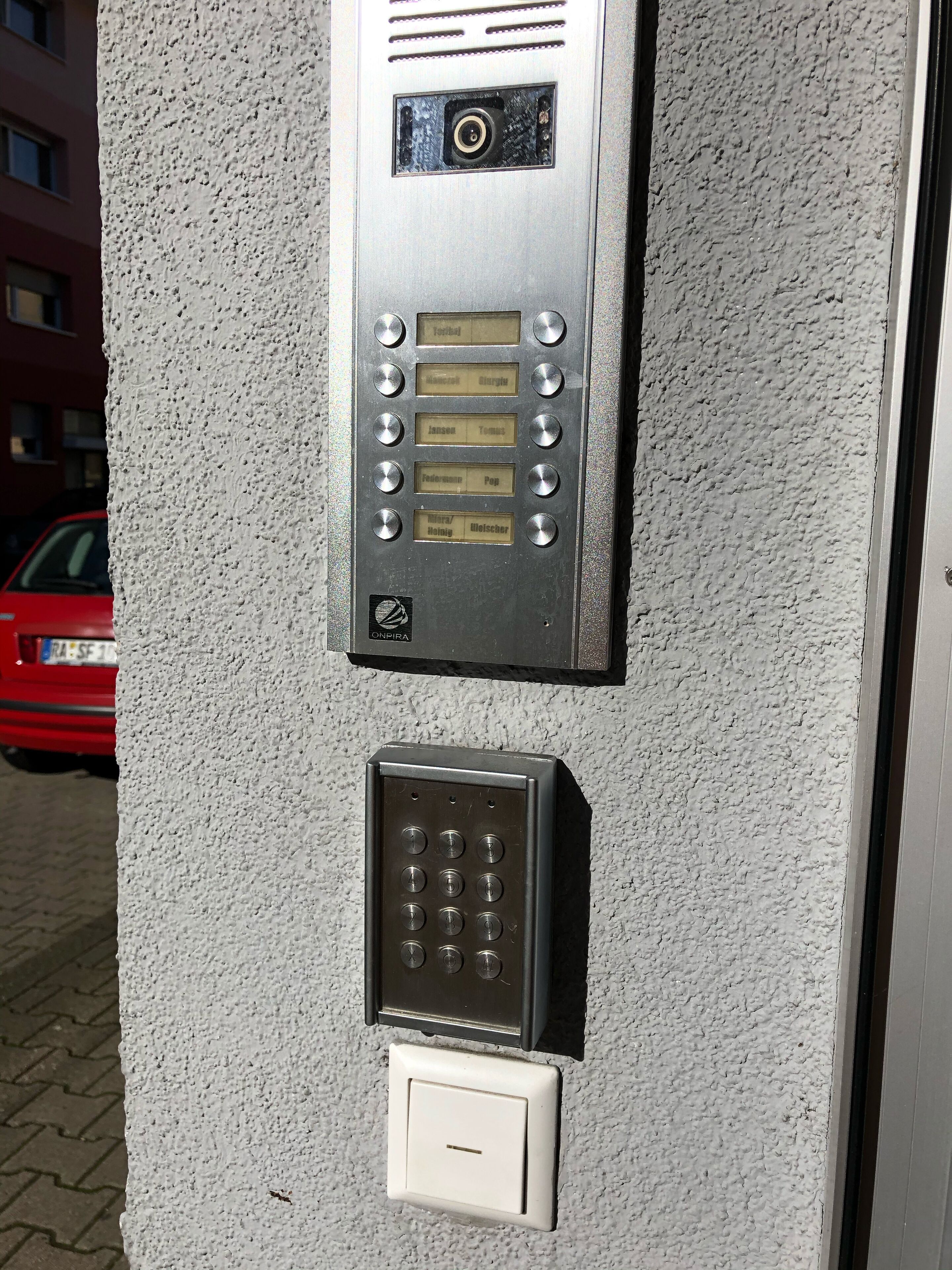 A wall-mounted intercom system with a keypad and a doorbell.