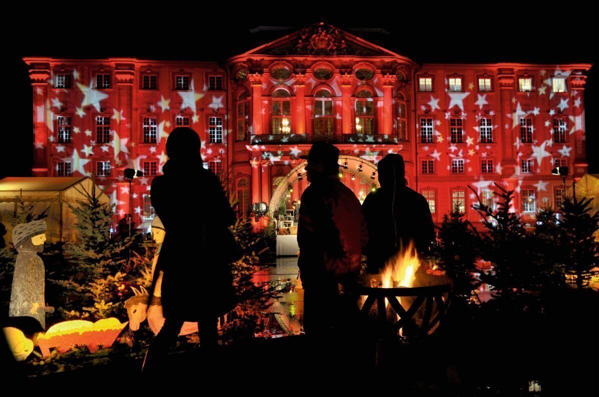 Un edificio de fachada roja con proyecciones de estrellas, rodeado de adornos navideños y fuego.