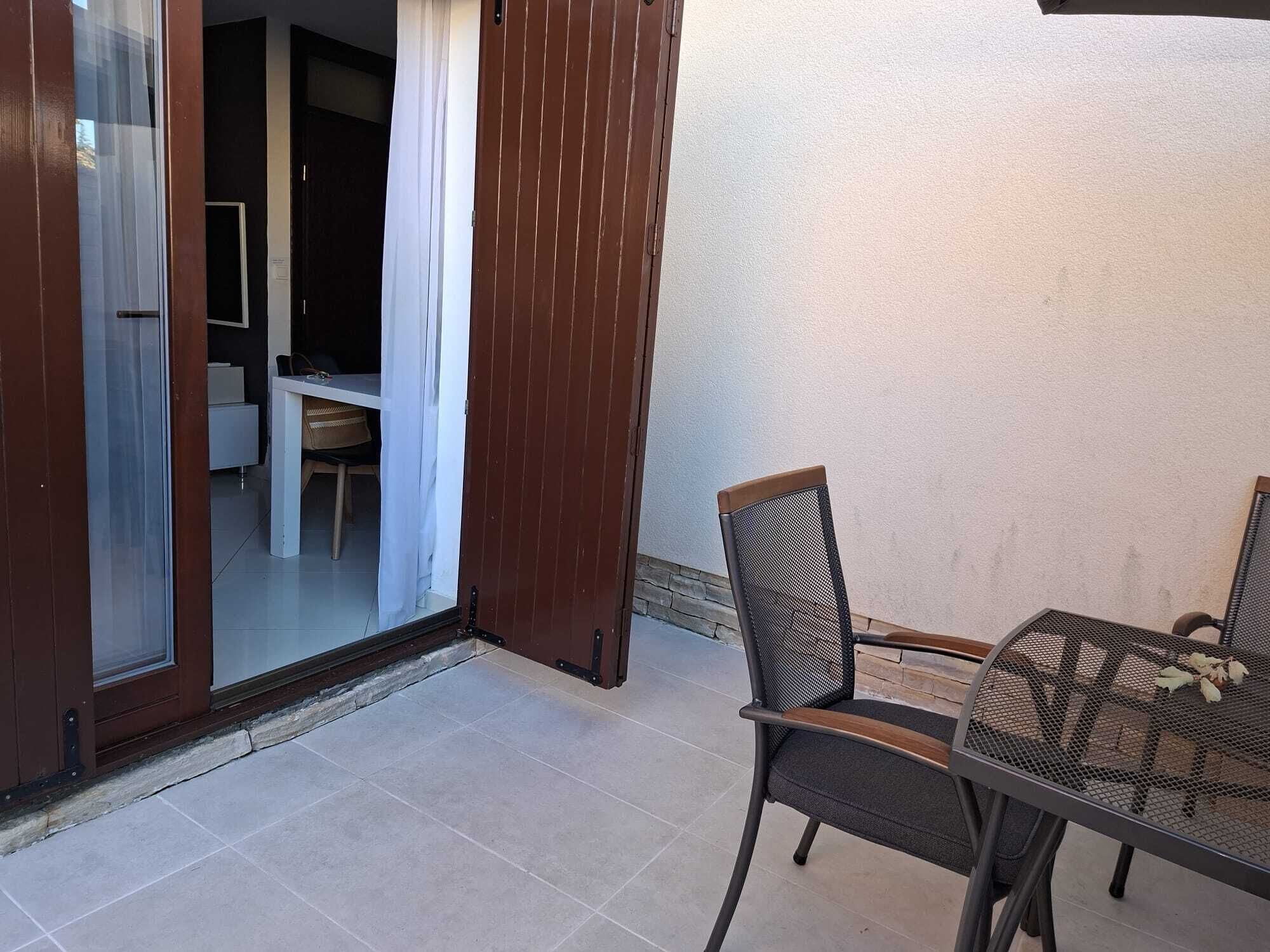 Eine Terrasse mit Tisch und Stühlen, eine Schiebetür zu einem Innenraum und eine weiße Wand.