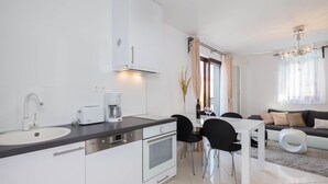 Een moderne keuken met witte kasten, een inbouwoven en een koffiezetapparaat. Er is een eethoek met een witte tafel en zwarte stoelen.