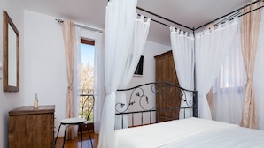A bedroom with a bed, a wooden dresser, a chair, and a balcony with curtains. - Villa Aurea (Čižići)