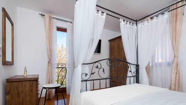 Een slaapkamer met een bed, een houten dressoir, een stoel en een balkon met gordijnen.