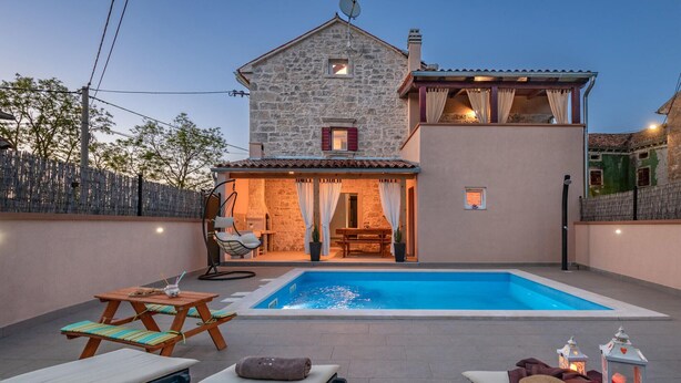 Una casa de pedra amb piscina, zona d'estar a l'exterior i un porxo cobert.