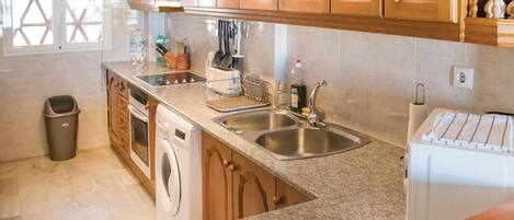 A kitchen with wooden cabinets, a stainless steel sink, a washing machine, and a toaster.