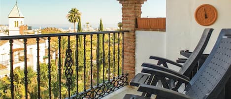 A balcony with a view of a cityscape, including a church and palm trees. There are two clocks on the wall and a metal railing.