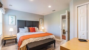 A bedroom with a bed, bedside tables, a bench, and a desk with a remote control.