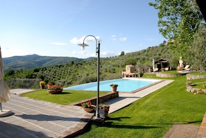 Una piscina con vistas a las colinas, una pérgola y plantas en macetas.