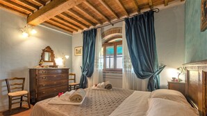 Een slaapkamer met een houten plafond, een bed met witte lakens, een houten dressoir en een stoel.