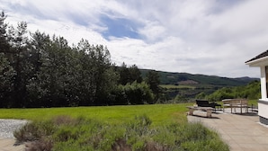 Ein Haus mit Terrasse, Sitzgelegenheiten im Freien und Blick auf eine grüne Landschaft und Hügel.