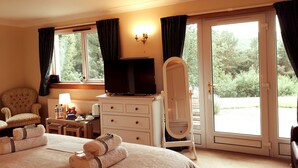 Ein Hotelzimmer mit Bett, Kommode, Sessel, Fernseher und einem Fenster mit Vorhängen.