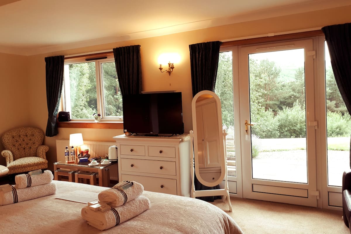 A hotel room with a bed, a dresser, a chair, a television, and a window with curtains.