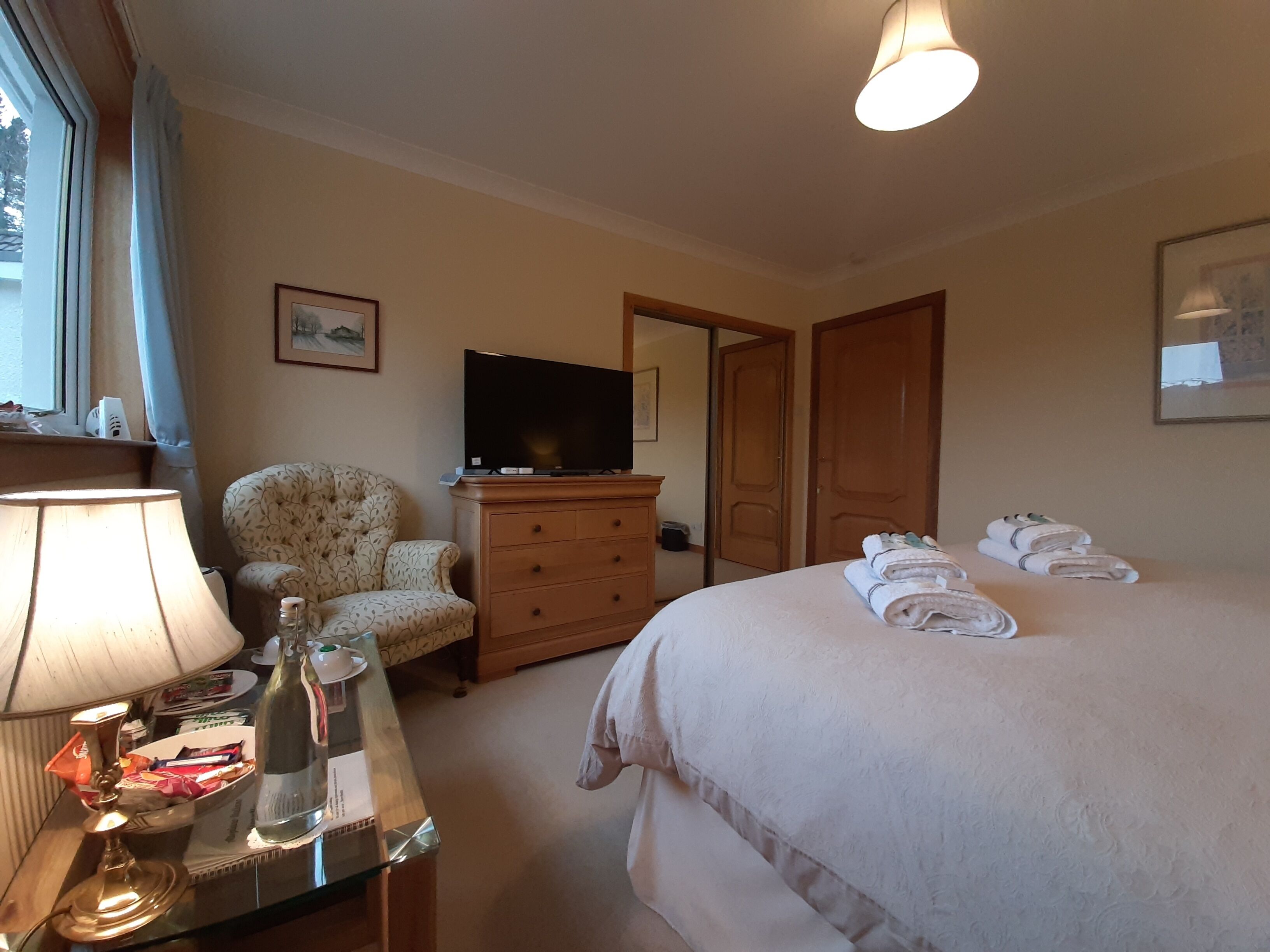 A hotel room with a bed, a chair, a dresser, a television, and a lamp.