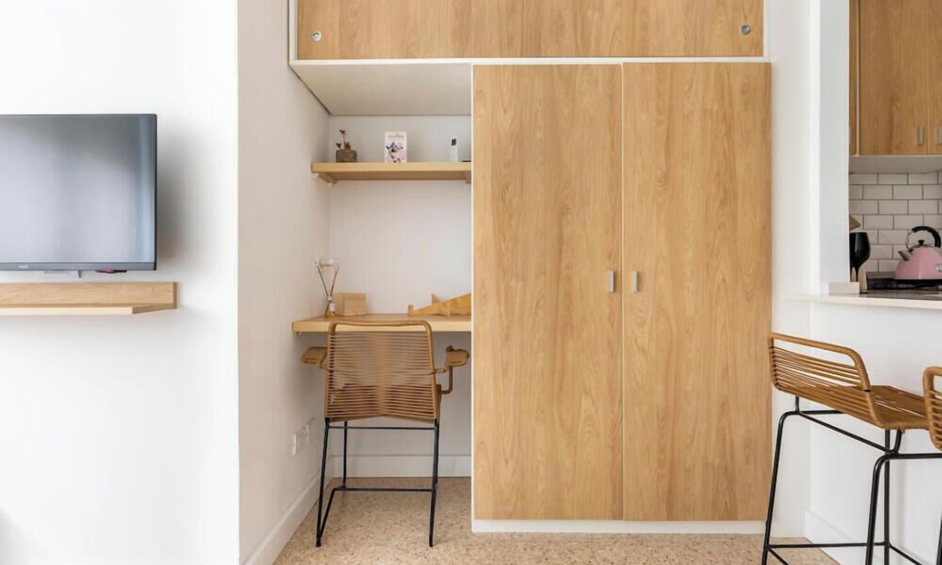 Een compacte keuken met houten kastjes, een aan de muur bevestigde televisie en twee barstoelen.