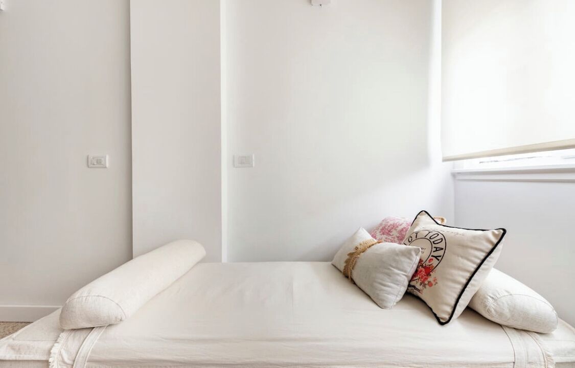 A minimalist bedroom with a bed, white walls, and a window.