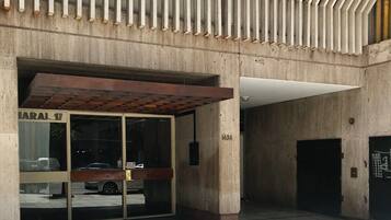 Una entrada de edificio con un gran ventanal, un toldo metálico y fachada de hormigón.