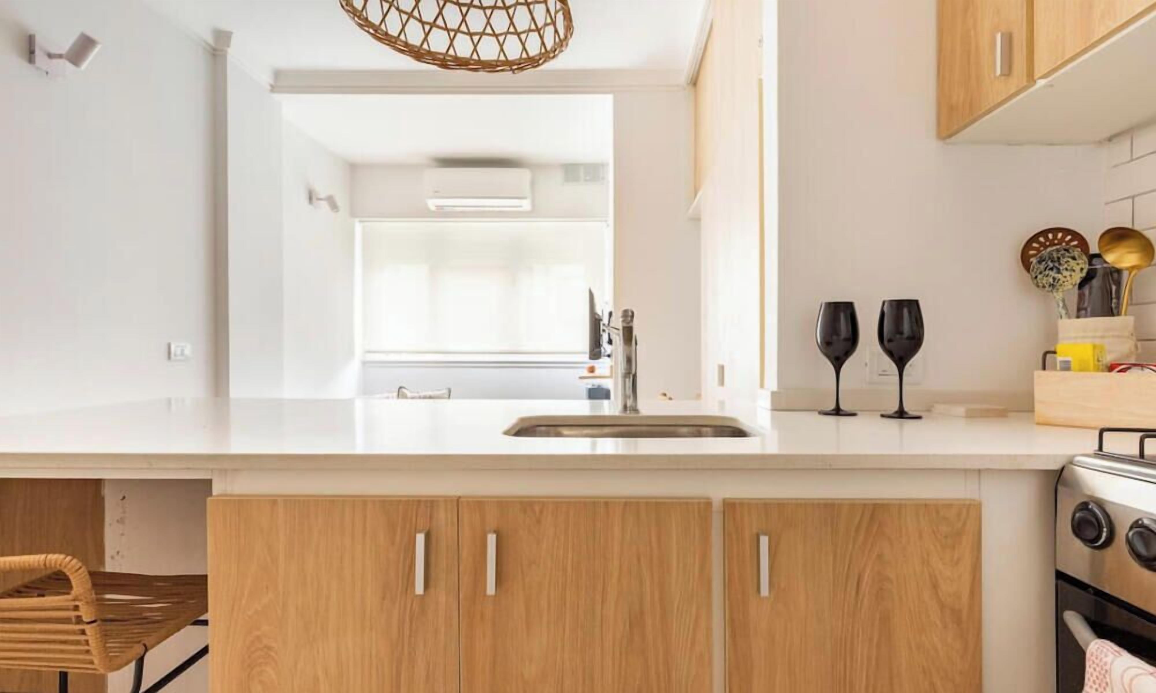 Una cocina moderna con armarios de madera, encimera blanca, pileta de acero inoxidable y estufa.