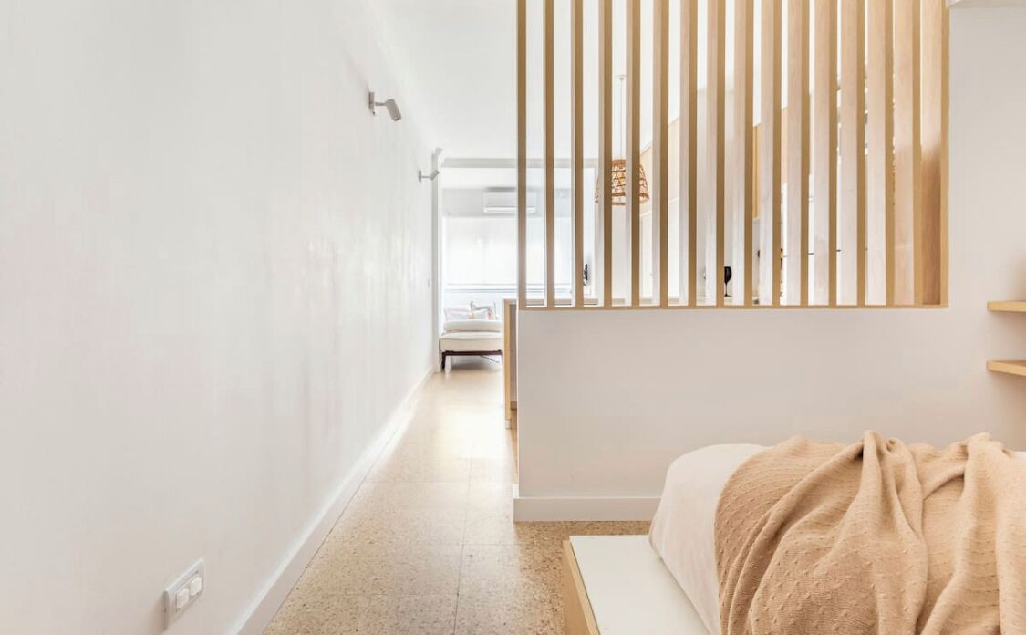 Habitación de hotel minimalista con cama, separador de listones de madera y vista al pasillo.