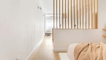 Habitación de hotel minimalista con cama, separador de listones de madera y vista al pasillo.