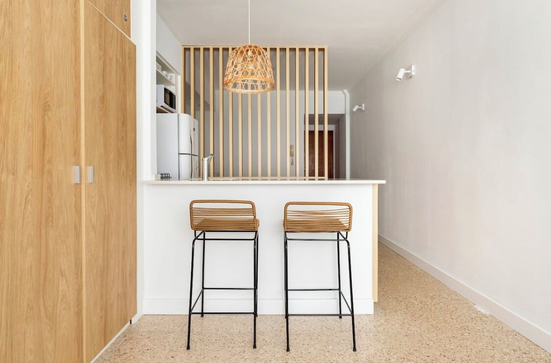 Una cocina moderna con dos taburetes de bar, una lámpara colgante y un separador de madera.