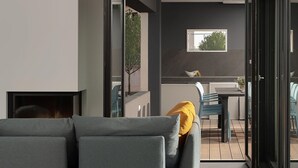 Ein modernes Wohnzimmer mit einem grauen Sofa, einem kleinen Tisch und einem Fenster mit Blick auf einen Balkon und einen Essbereich.