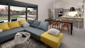Ein modernes Wohnzimmer mit einem grauen Sofa, einem gelben Pouf und einem Essbereich mit einem schwarzen Tisch und Stühlen.