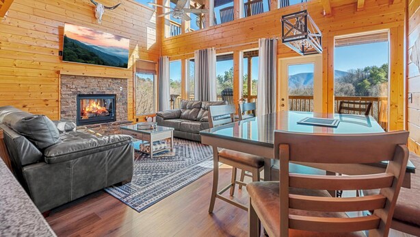 A spacious log cabin with a fireplace, leather furniture, and large windows offering scenic views. - 20-Mile View, Hot Tub, Game Room, Waterfall (Sevierville)